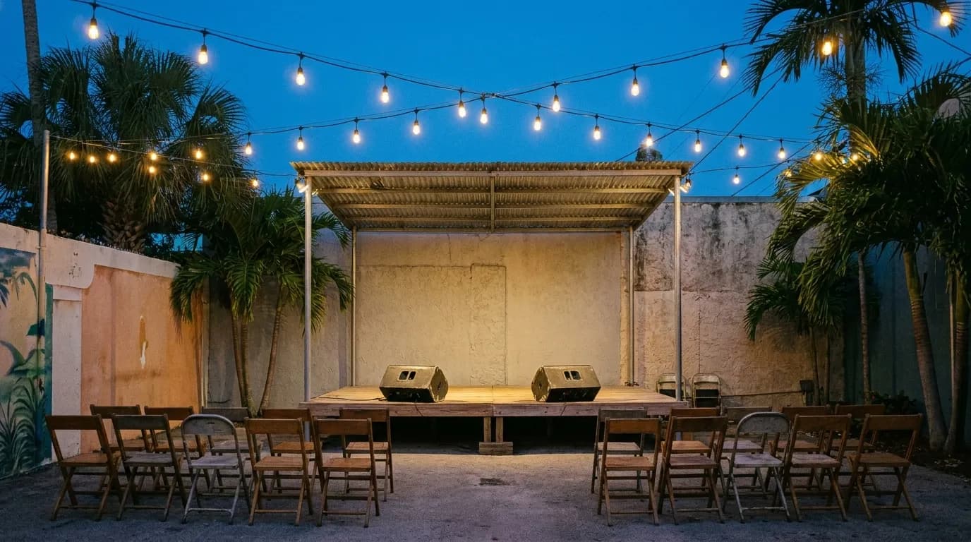 An outdoor stage under string lights in a courtyard with empty folding chairs facing it