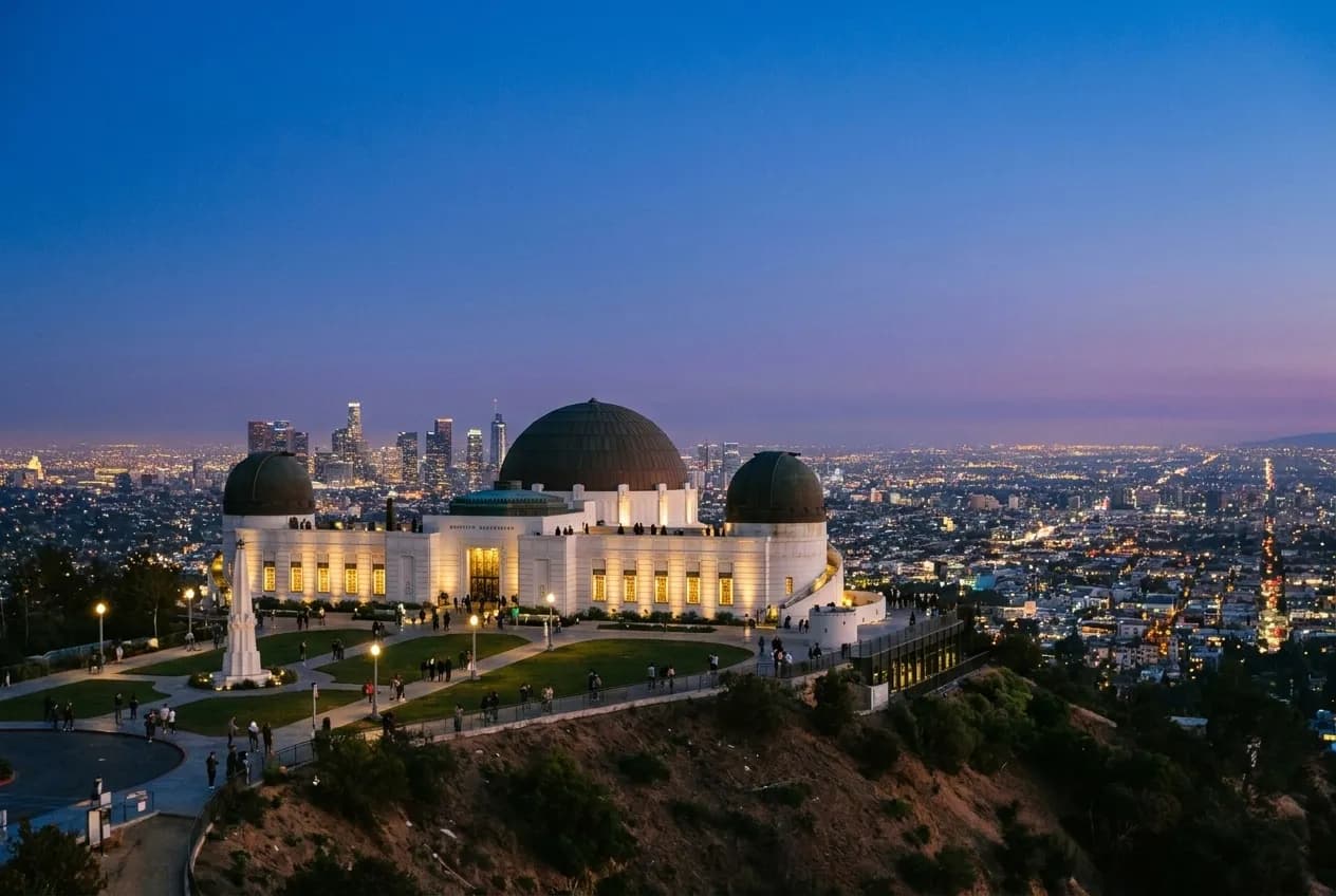 Griffith Observatory illuminated at twilight with Los Angeles city lights visible in the distance.