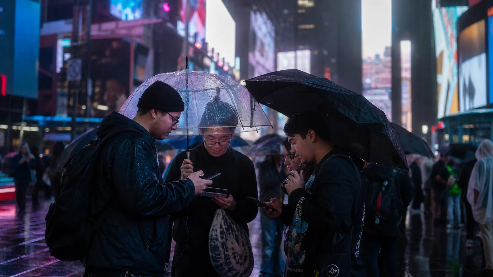 Gamers checking phones on a rainy night in Times Square while waiting for gaming news.