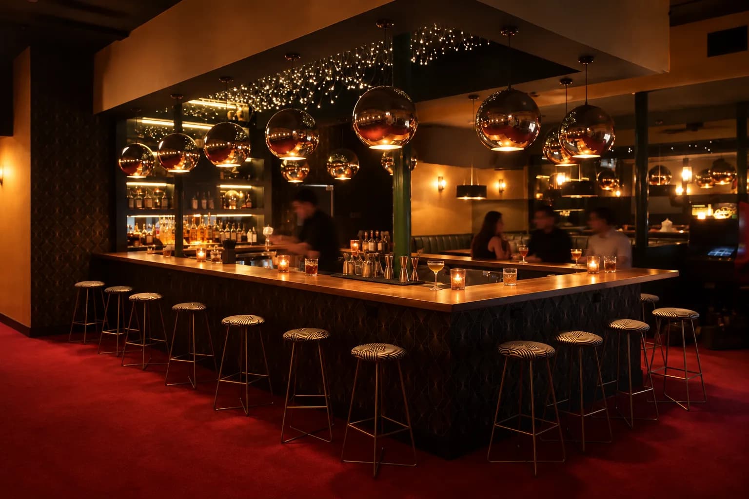 A U-shaped wooden bar under mirrored copper globe lamps with red carpet and striped stools during early evening happy hour
