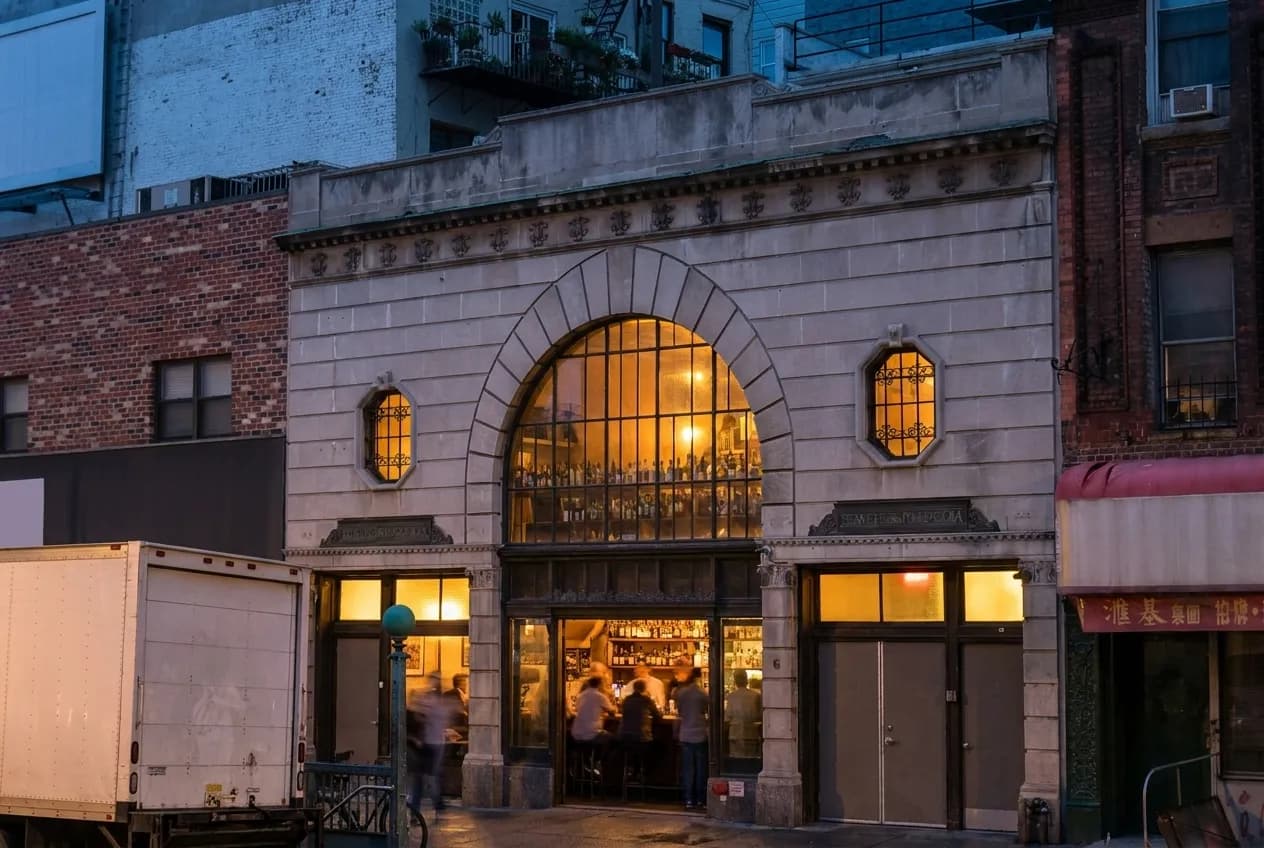 New York City bar exterior at dusk with warm light and people inside