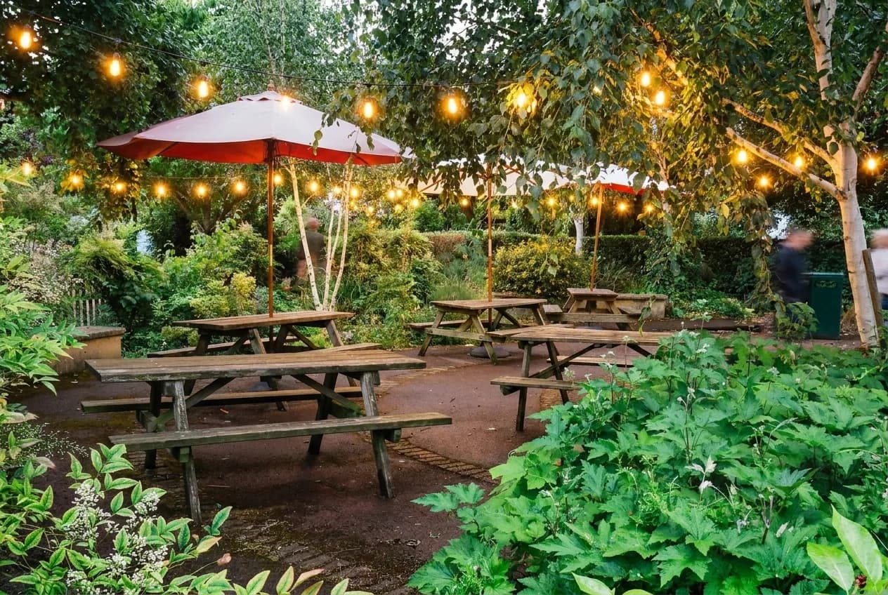 An outdoor beer garden at dusk with picnic tables and string lights