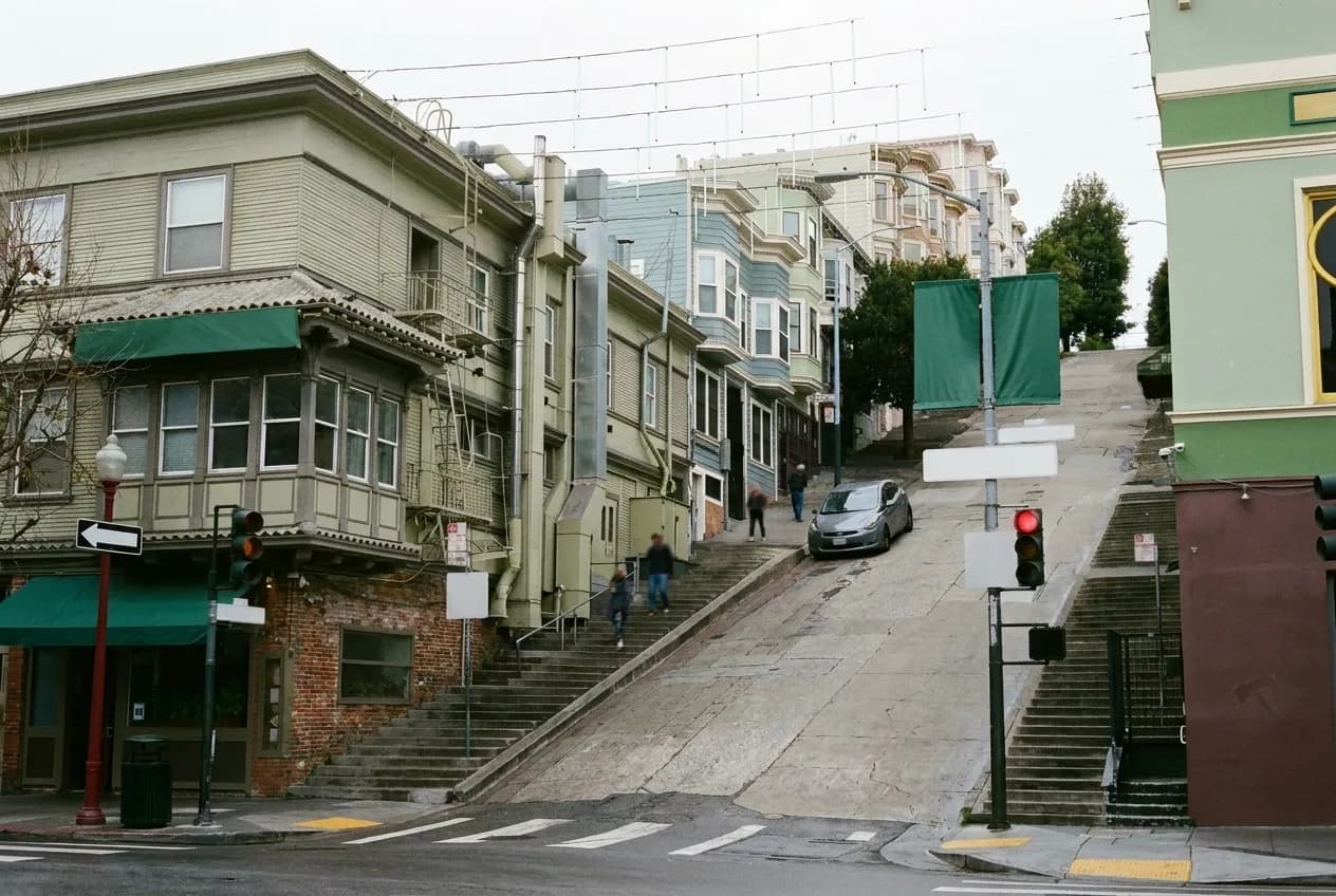 A steep San Francisco street in late afternoon with bar awnings and parked cars