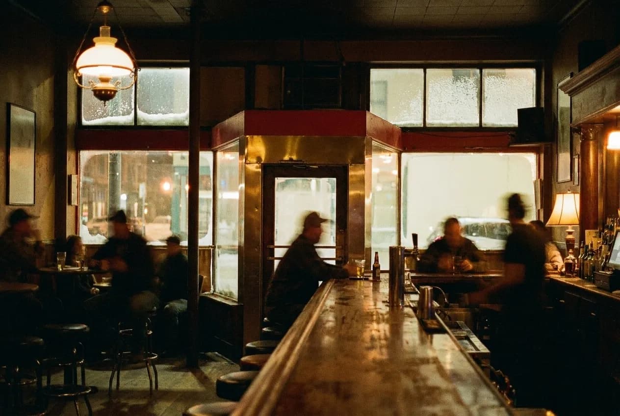 A dimly lit dive bar interior with a long wooden bar and stools