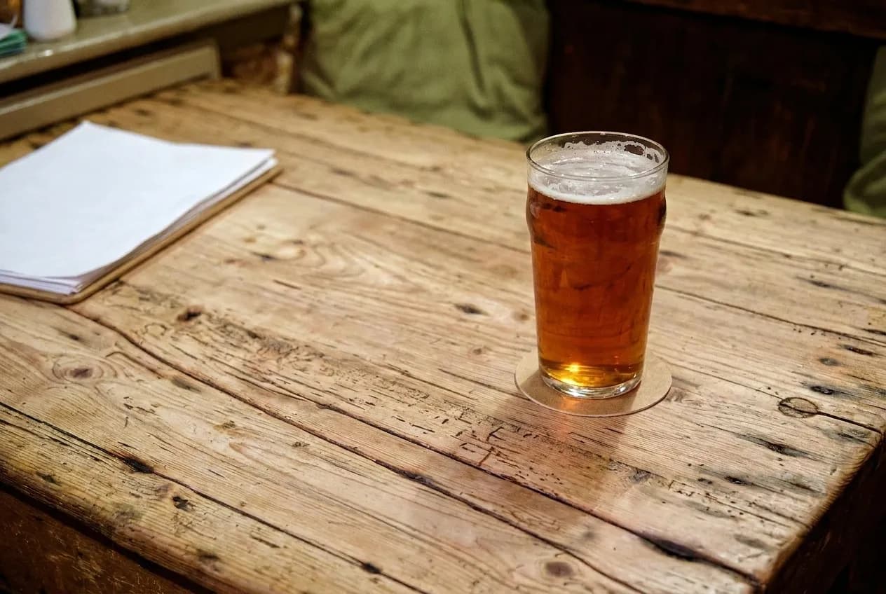 A pint of beer on a scarred wooden bar with a coaster