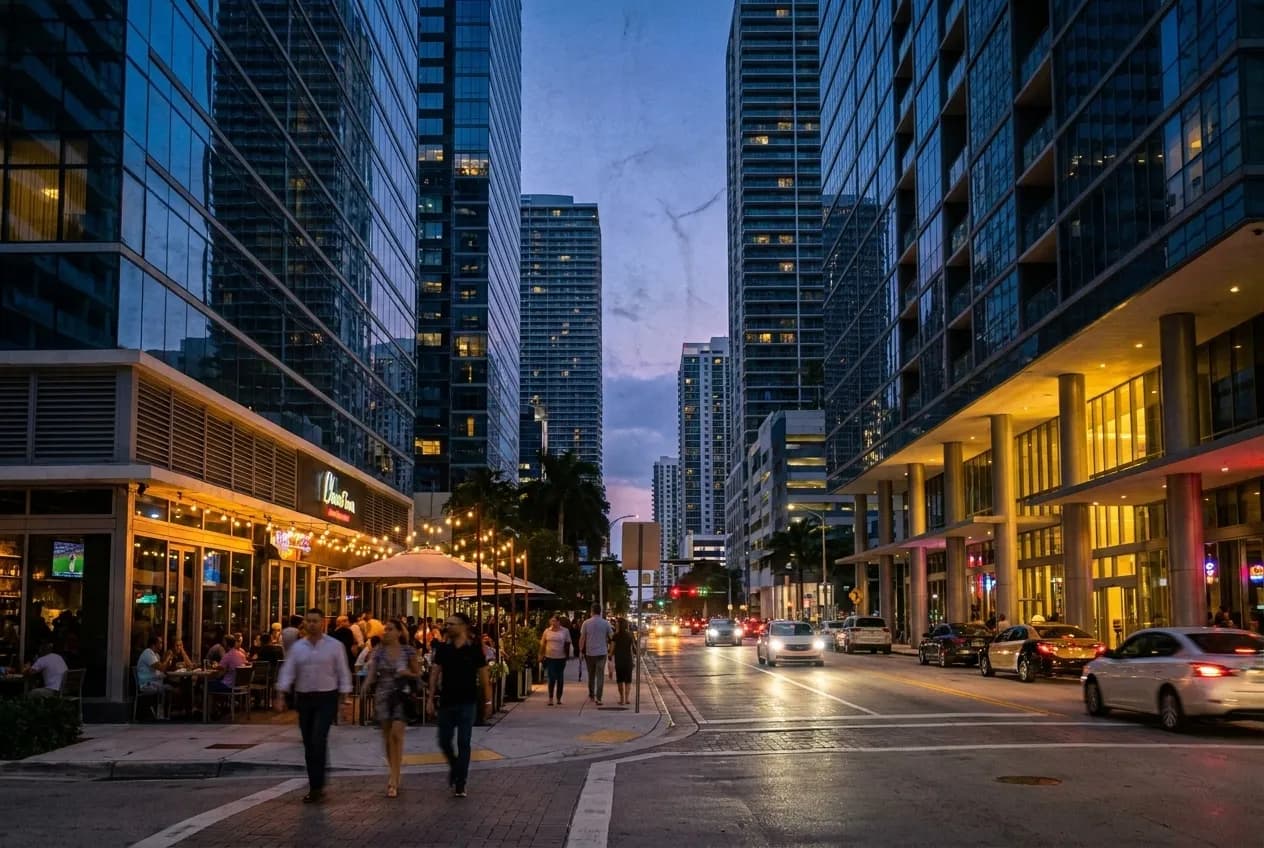 Glassy Brickell high-rise towers at dusk with lit street-level patios and pedestrian traffic along Miami Avenue.