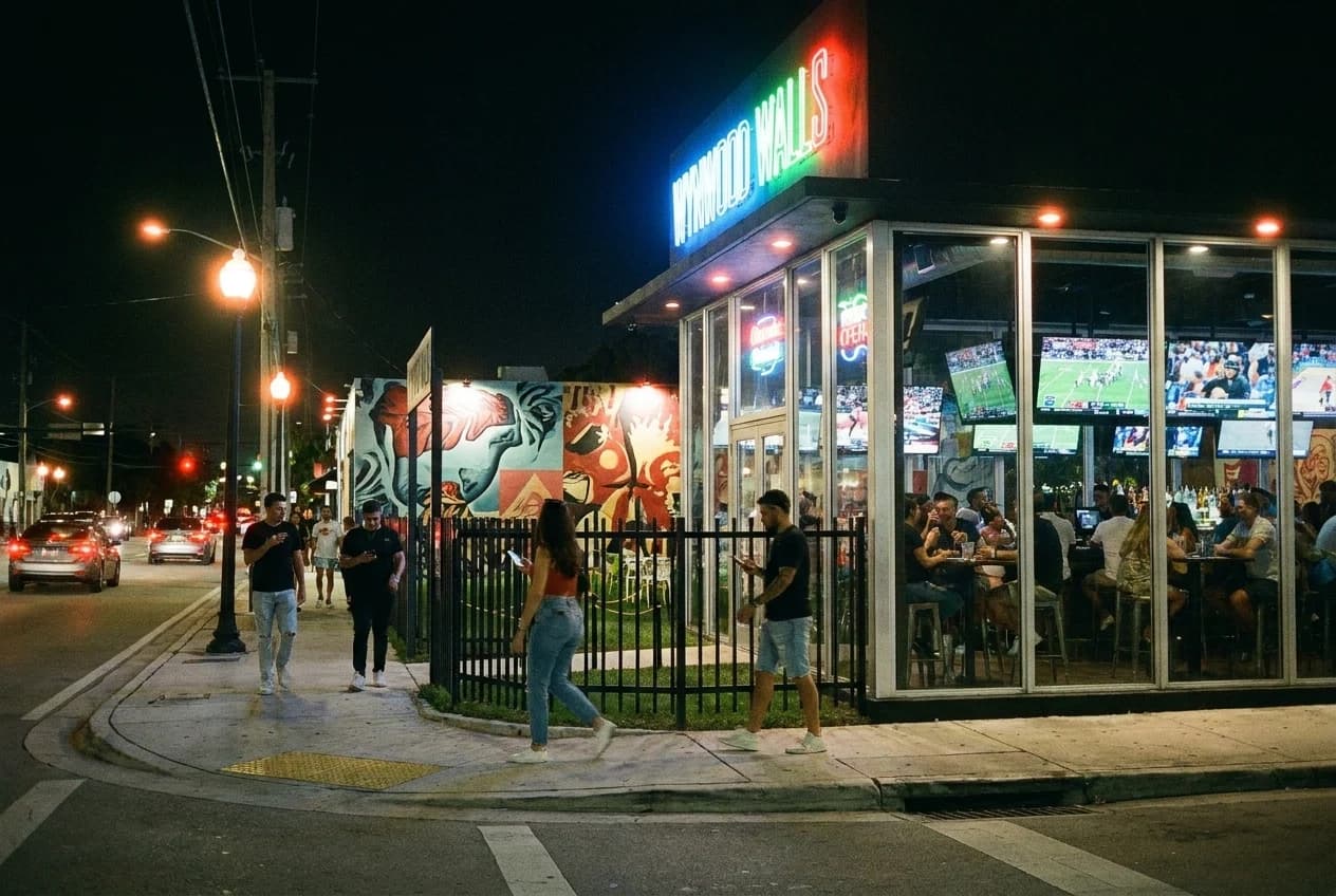 Wynwood sports bar exterior at night with TVs visible through windows and neon signage