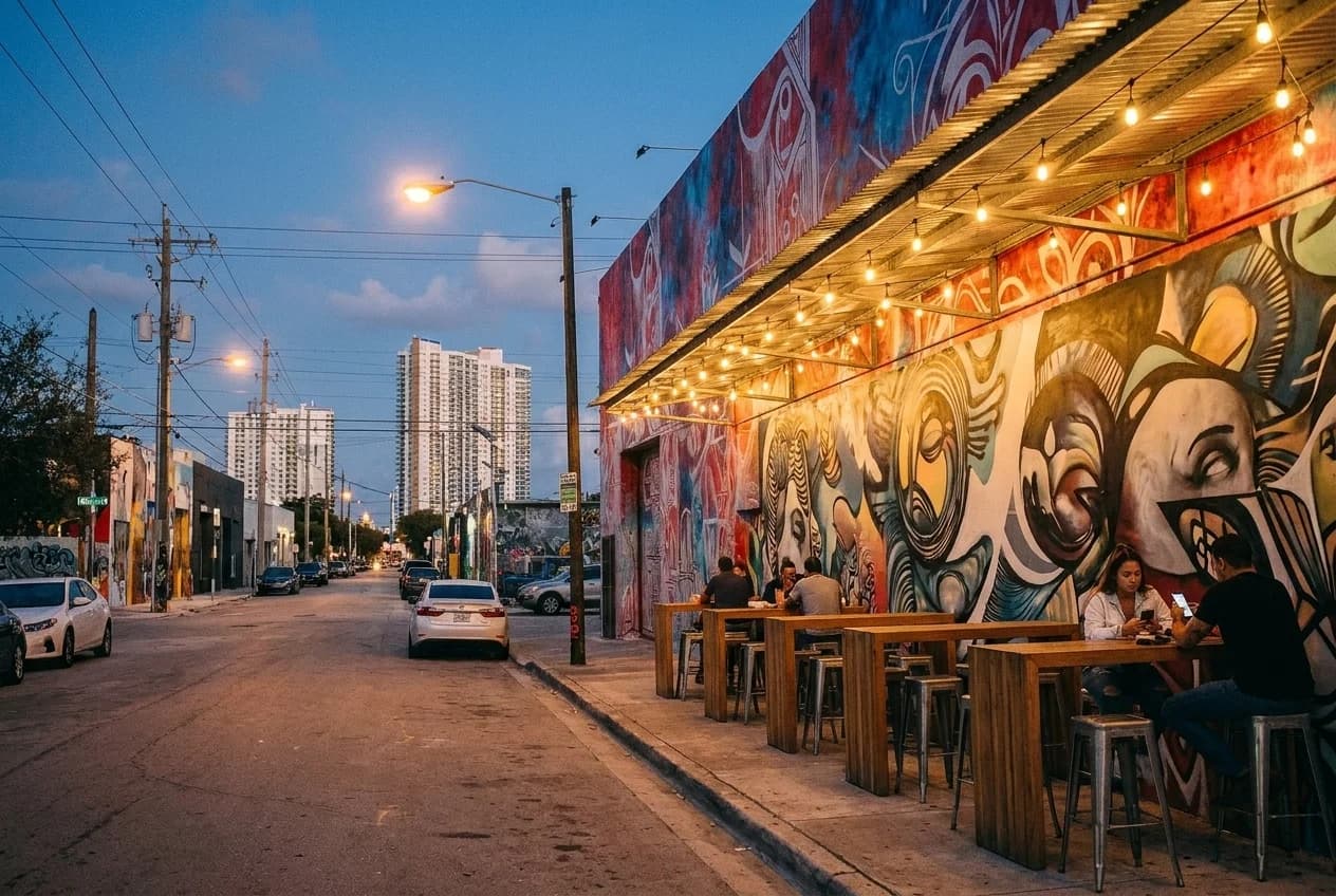 Outdoor tables under metal awning at Wynwood bar with mural wall and string lights at dusk