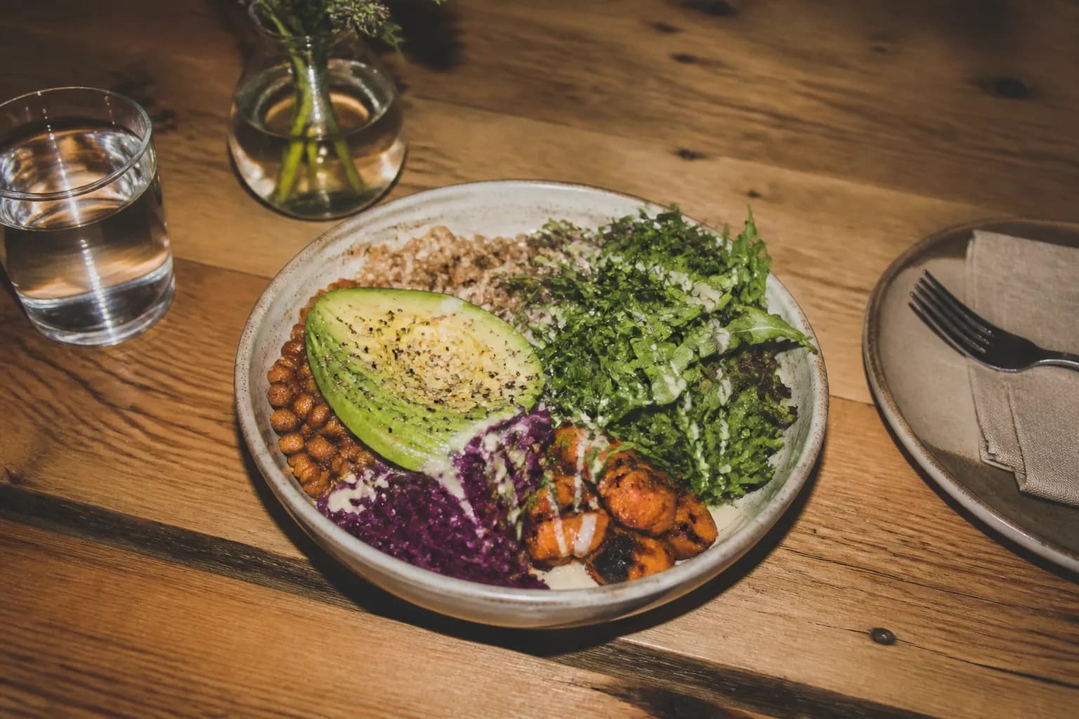 A fresh grain bowl with greens and avocado on a wood table