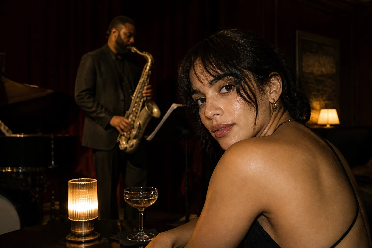 A dim jazz club with a musician playing under warm amber stage light