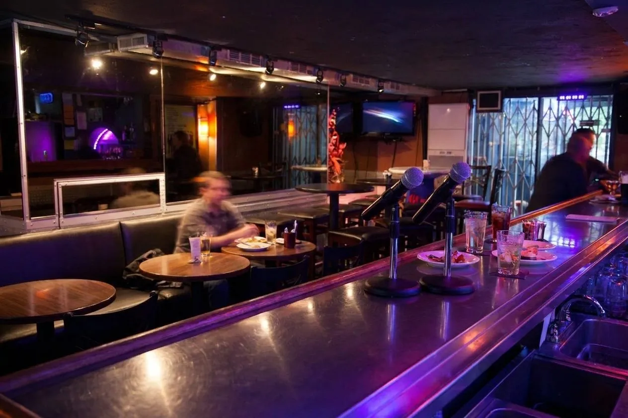 Neon-lit karaoke lounge counter with microphones and booth seating