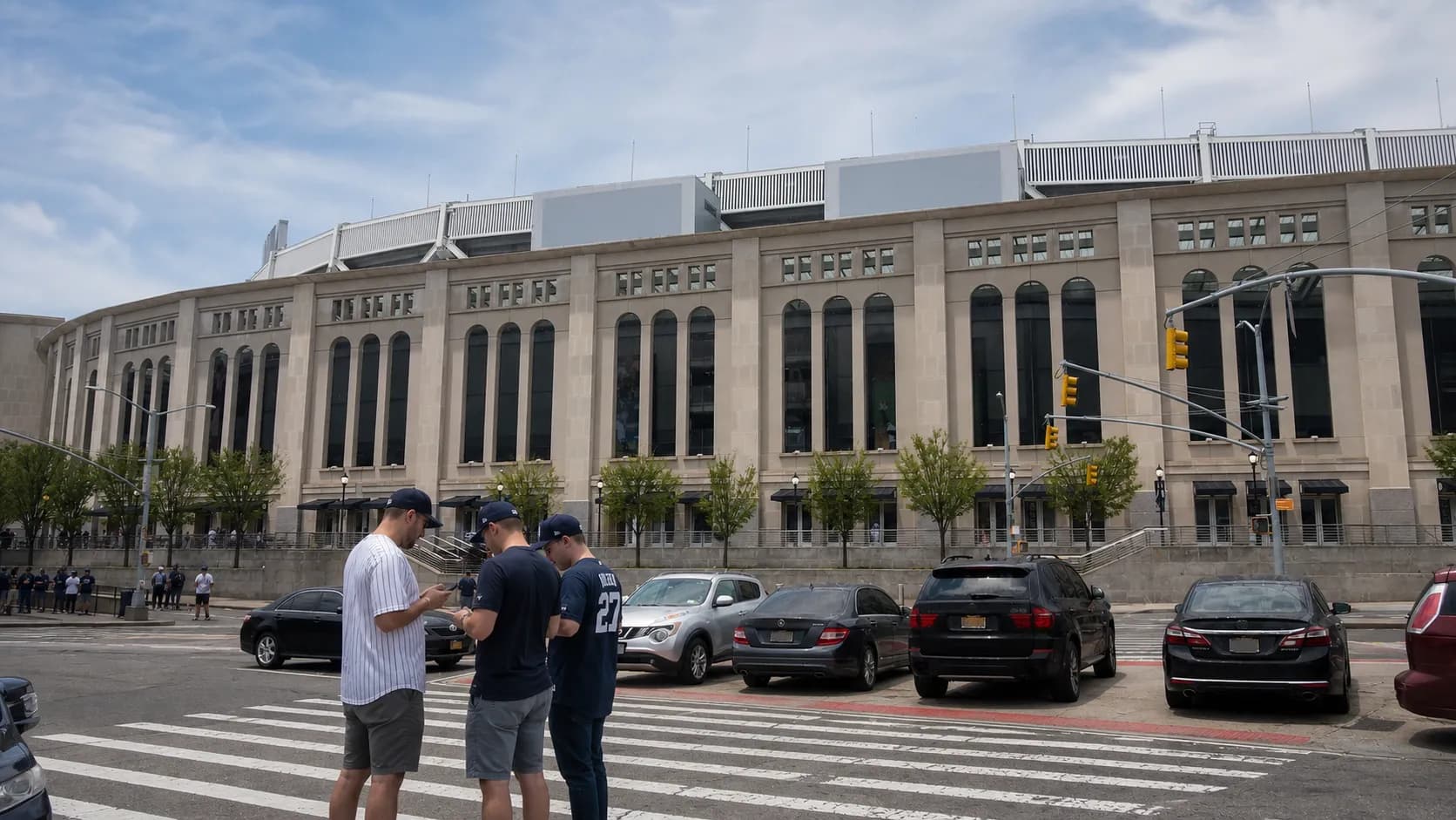 Fans outside a Bronx baseball stadium checking phones for game broadcast information.