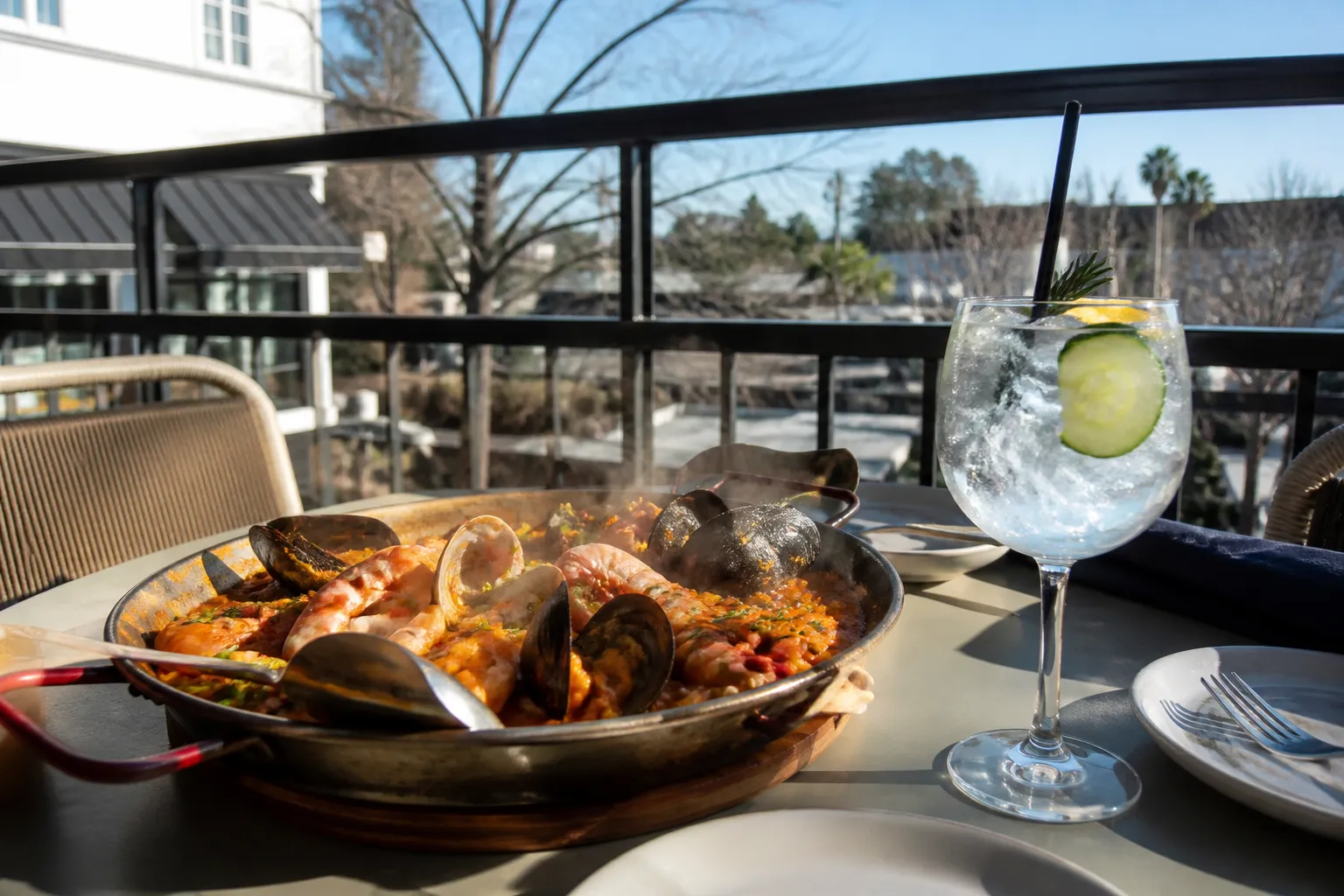 Seafood paella and a gin and tonic cocktail served on a sunny outdoor restaurant patio.