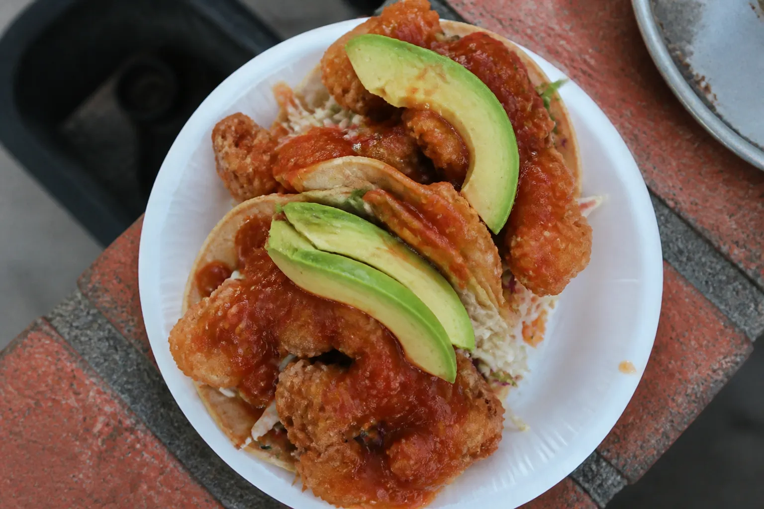 Crispy fried shrimp tacos served on a paper plate with red salsa and avocado.