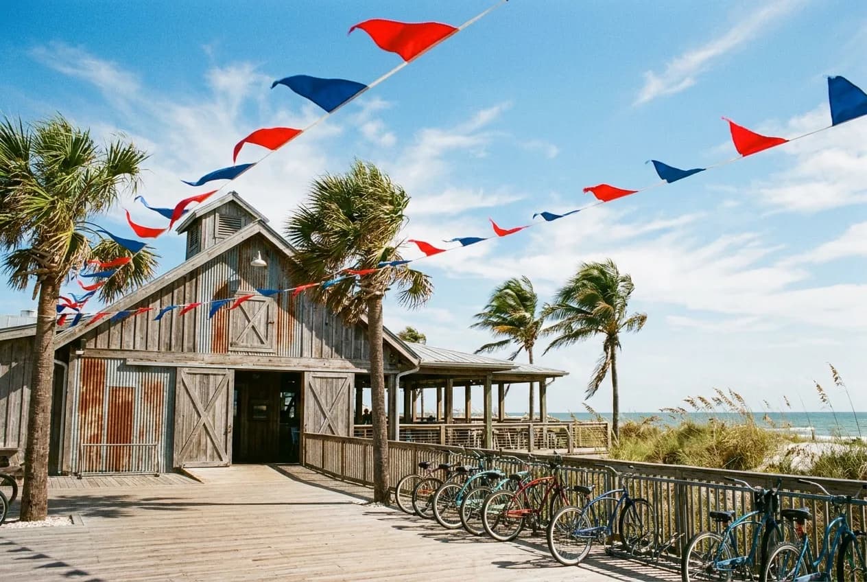 A beach-adjacent bar with scarlet and blue flags fluttering against a sunny boardwalk sky