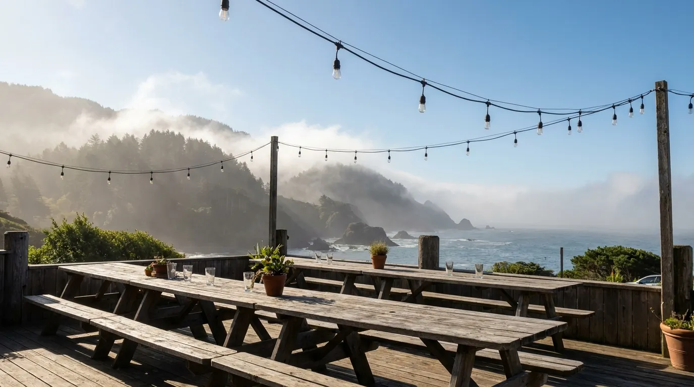 A sunlit patio with picnic tables, string lights off, and morning fog burning away