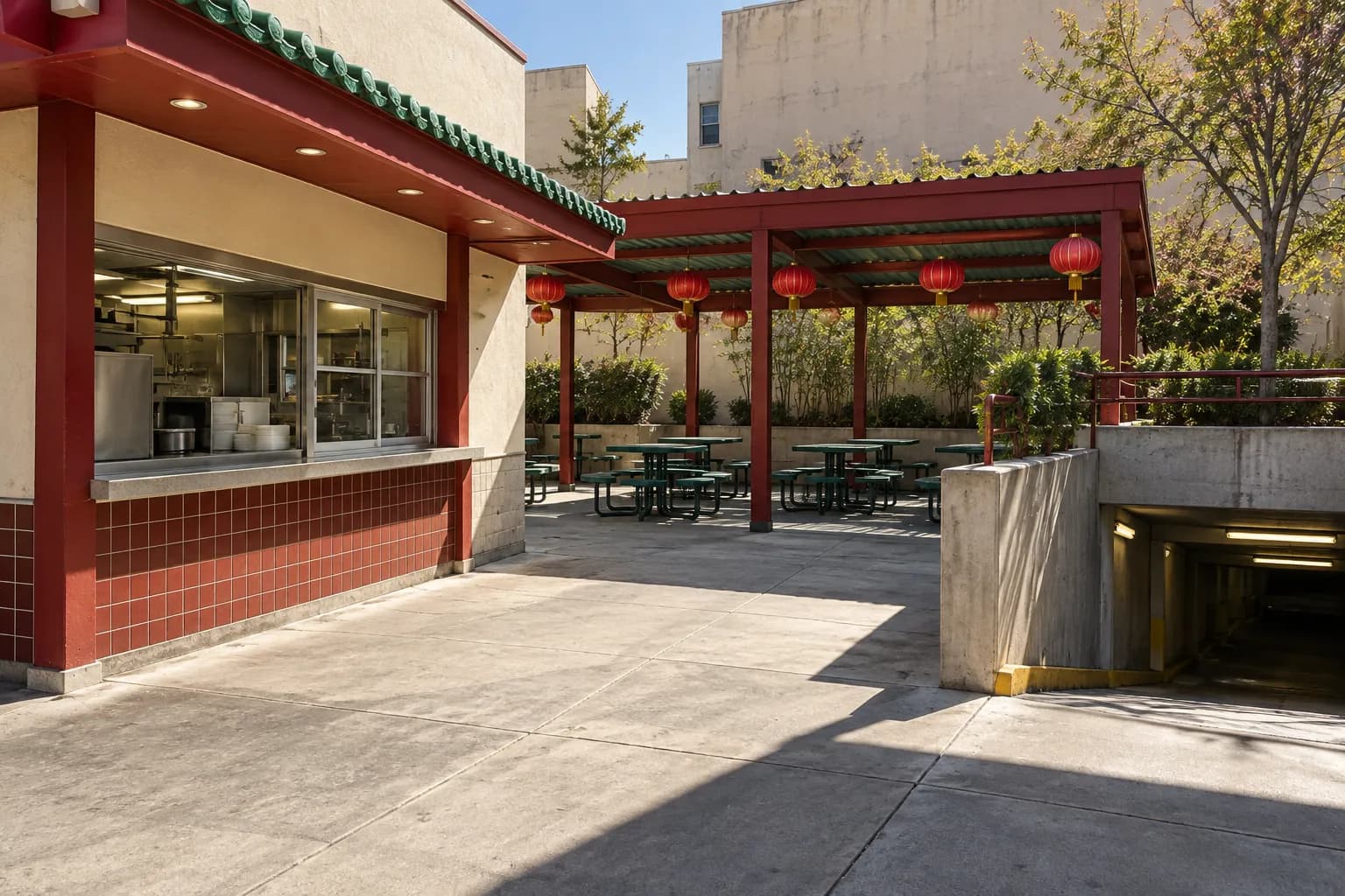 A street-level architectural view of a low-rise Chinatown plaza with a walk-up food counter, covered outdoor seating and a paid underground garage entrance, photographed in daylight.