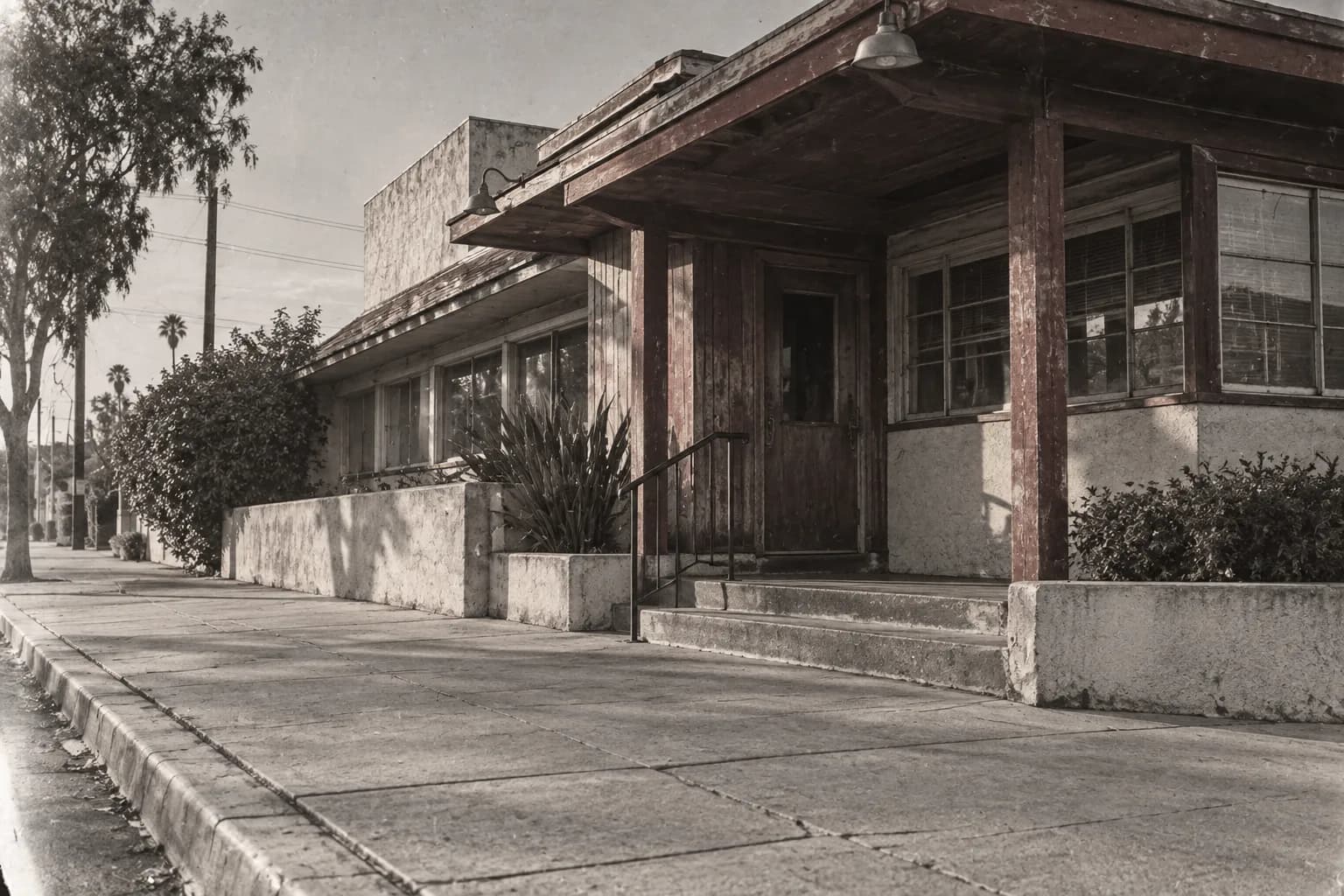 Wide street-level photograph of a historic low-rise restaurant approach, pale afternoon light across pavement, dark wood and cream walls, with a clear route leading towards the entrance.