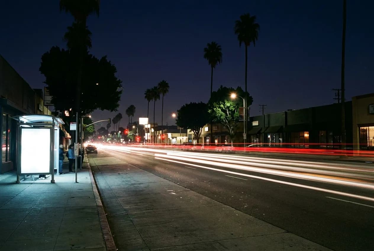 A wide boulevard in East Hollywood at night with low buildings, traffic and palm silhouettes