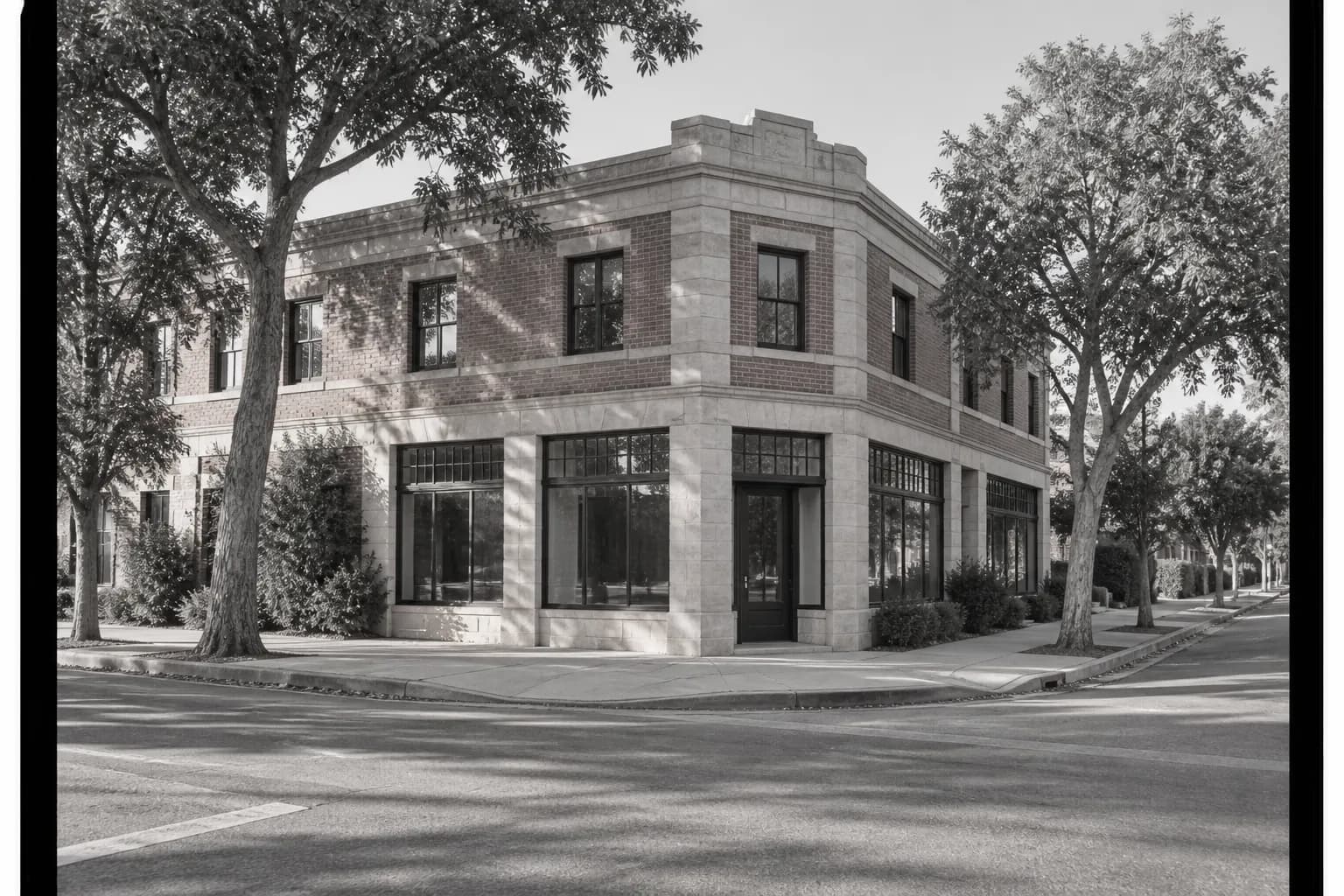 Wide street-level photograph of a two-story sandstone-brick corner building at a Los Feliz intersection, with broad pavement, mature trees and muted afternoon light.
