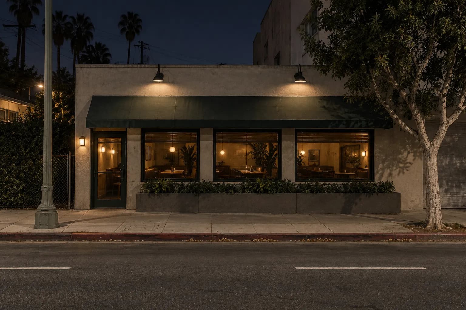 A low urban restaurant frontage at night on a Los Angeles street, with warm light behind dark windows, concrete pavement and muted amber and green tones, viewed straight on with no visible diners.