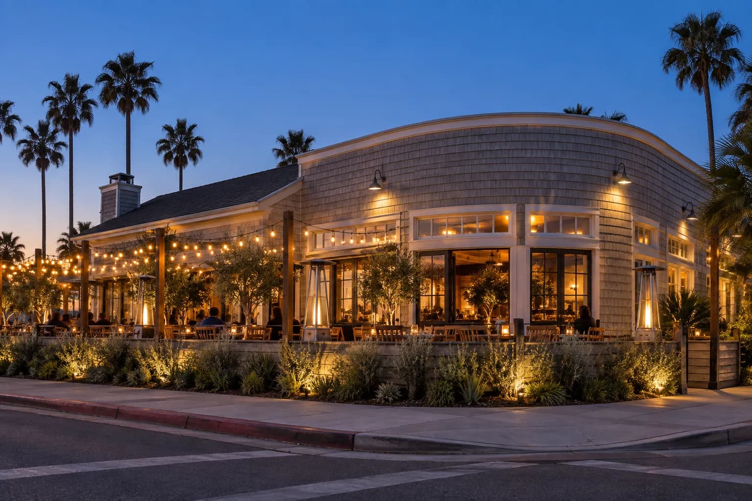 A low shingle-clad building on a corner lot with a lit patio wrapping around the front