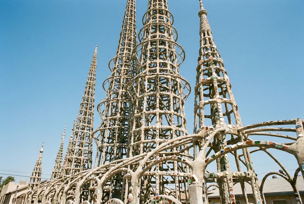 Tall open lattice spires of steel wrapped in mortar and set with fragments of tile against a blue sky