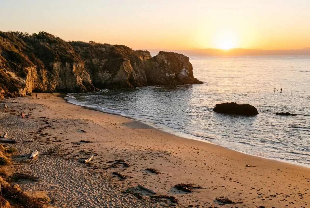 A wide stretch of Pacific coastline in the afternoon with cliffs behind the sand