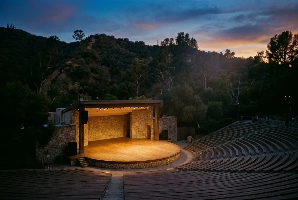 An outdoor amphitheatre stage lit against hillside trees at dusk