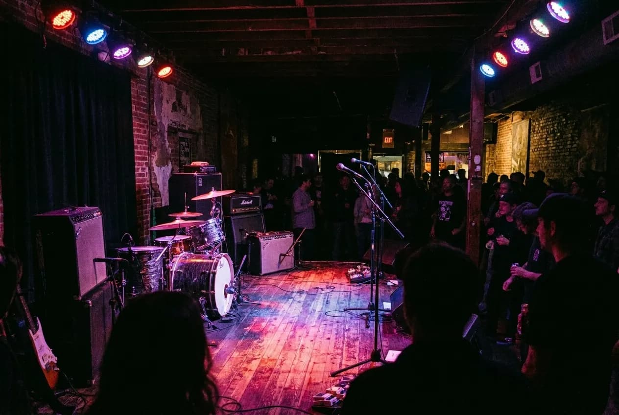 A small club stage under coloured lights, the room dark beyond it