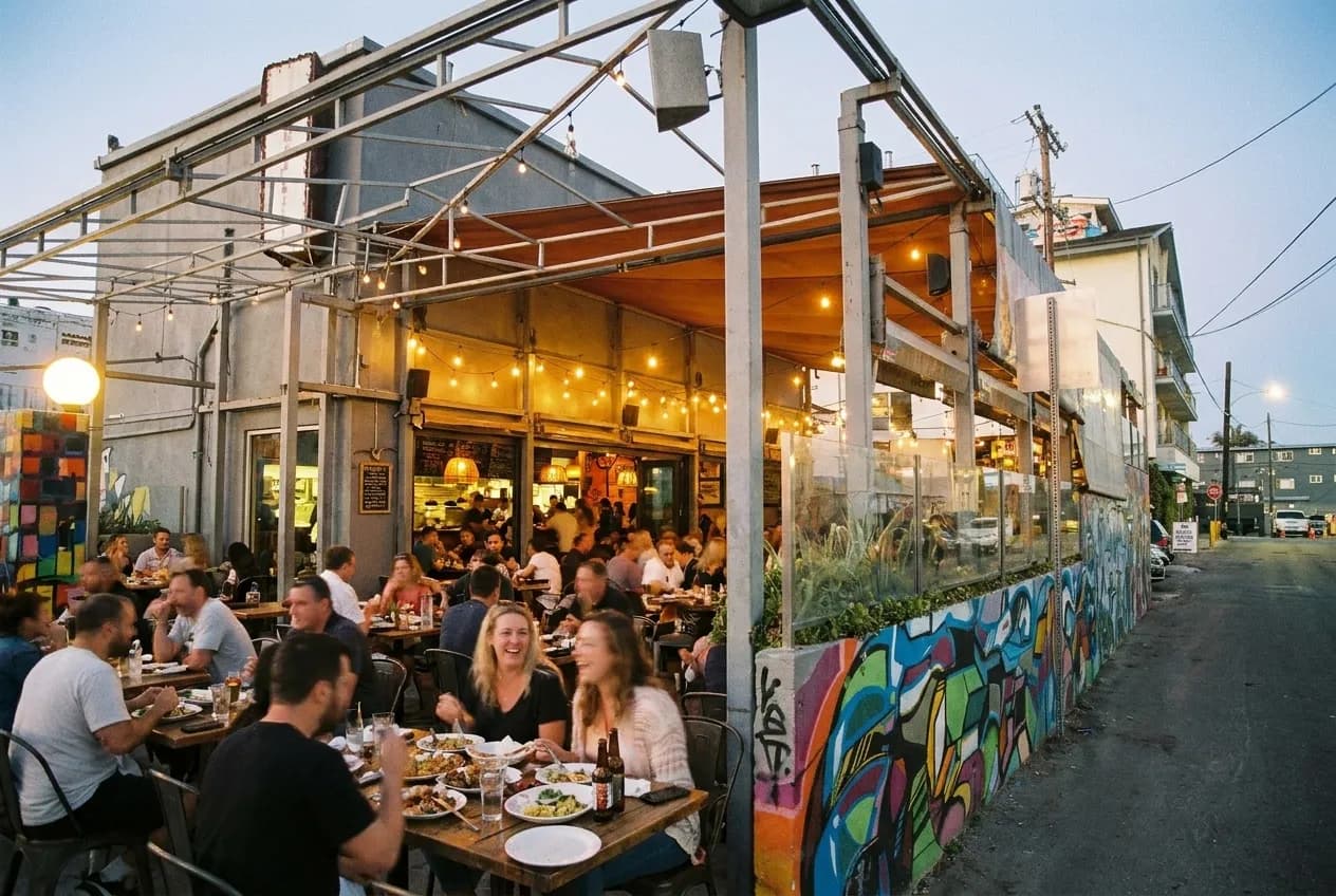 A restaurant with its front open to the street, tables filling at dusk