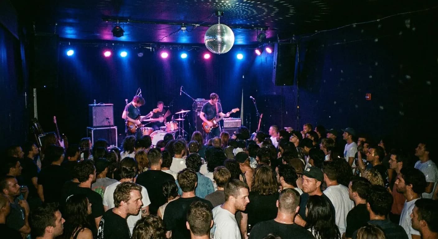 A compact Los Angeles venue stage during a set with blue and magenta lighting and a crowd of about a hundred packed close