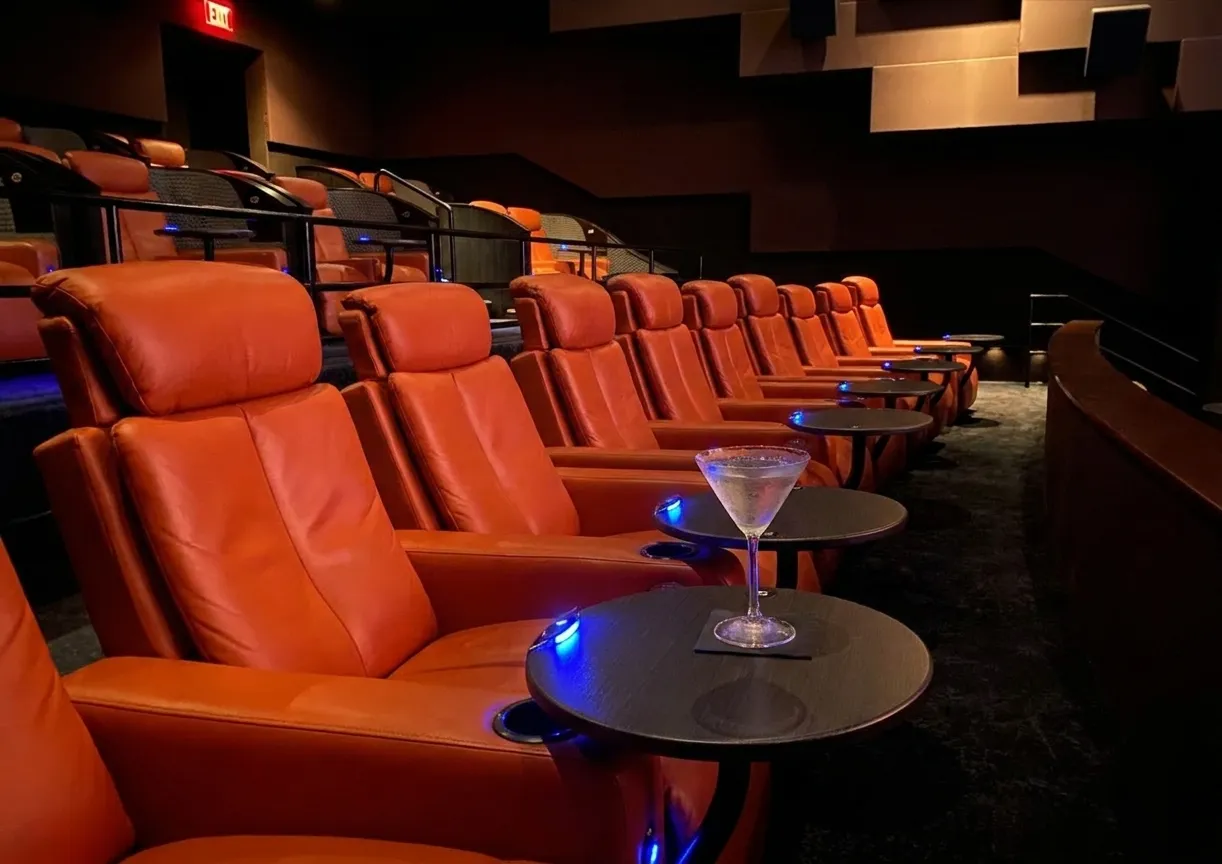 Leather recliner seat with cocktail glass on armrest tray inside a darkened movie theater auditorium