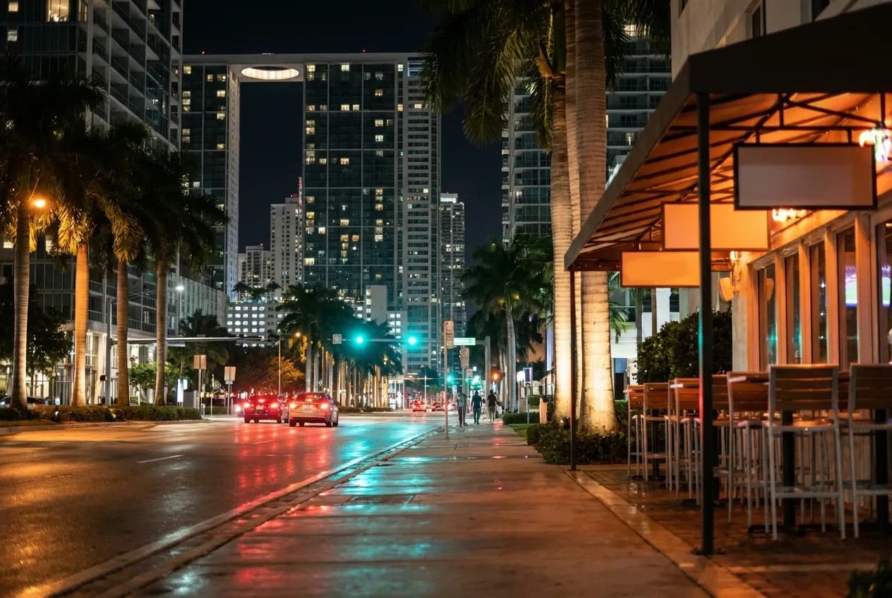 Brickell avenue in Miami at night with wet asphalt, lit palms and an empty bar terrace glowing amber on the right