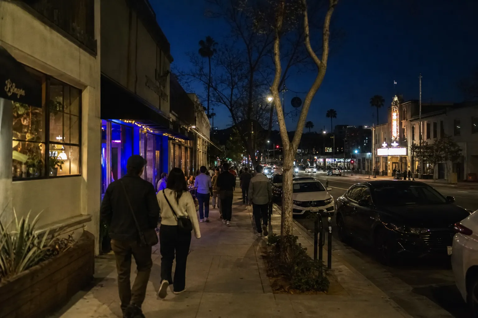 People walking through Los Feliz after dark near taco shops and theaters