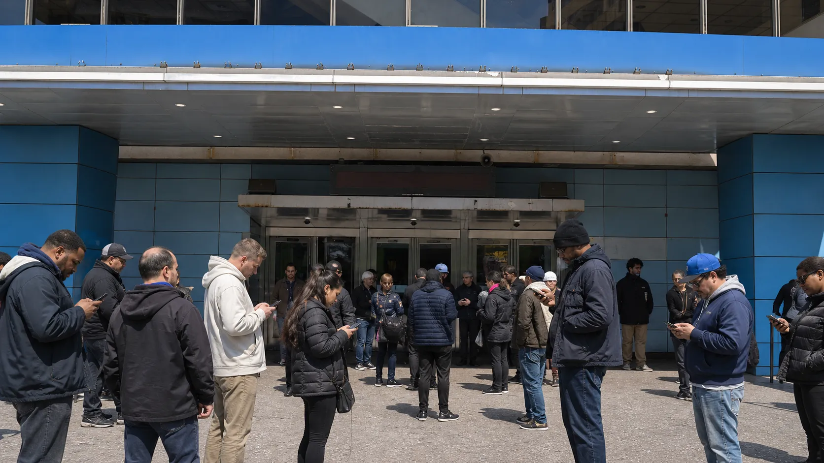 Basketball fans checking phones outside a large Manhattan arena.