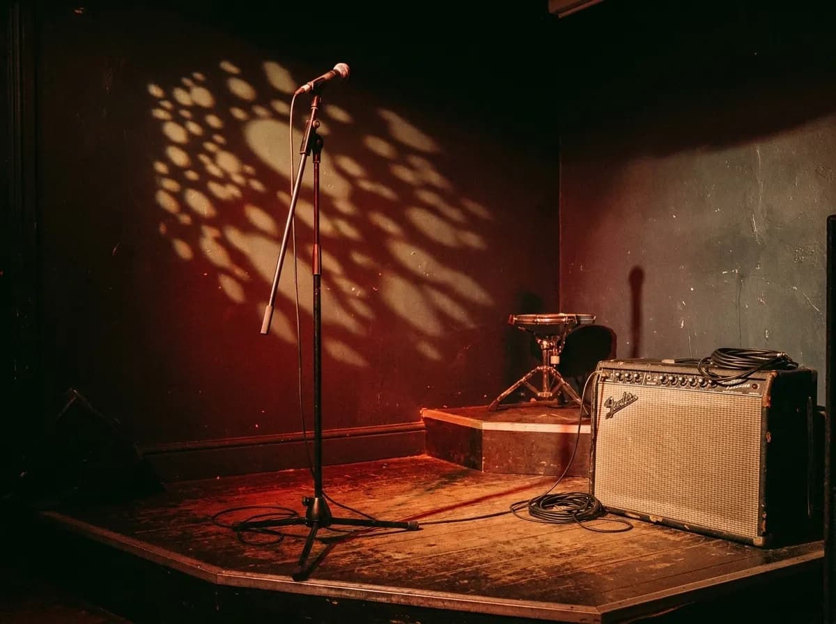 A small stage with a microphone stand, amplifier and warm red lighting in a narrow bar room