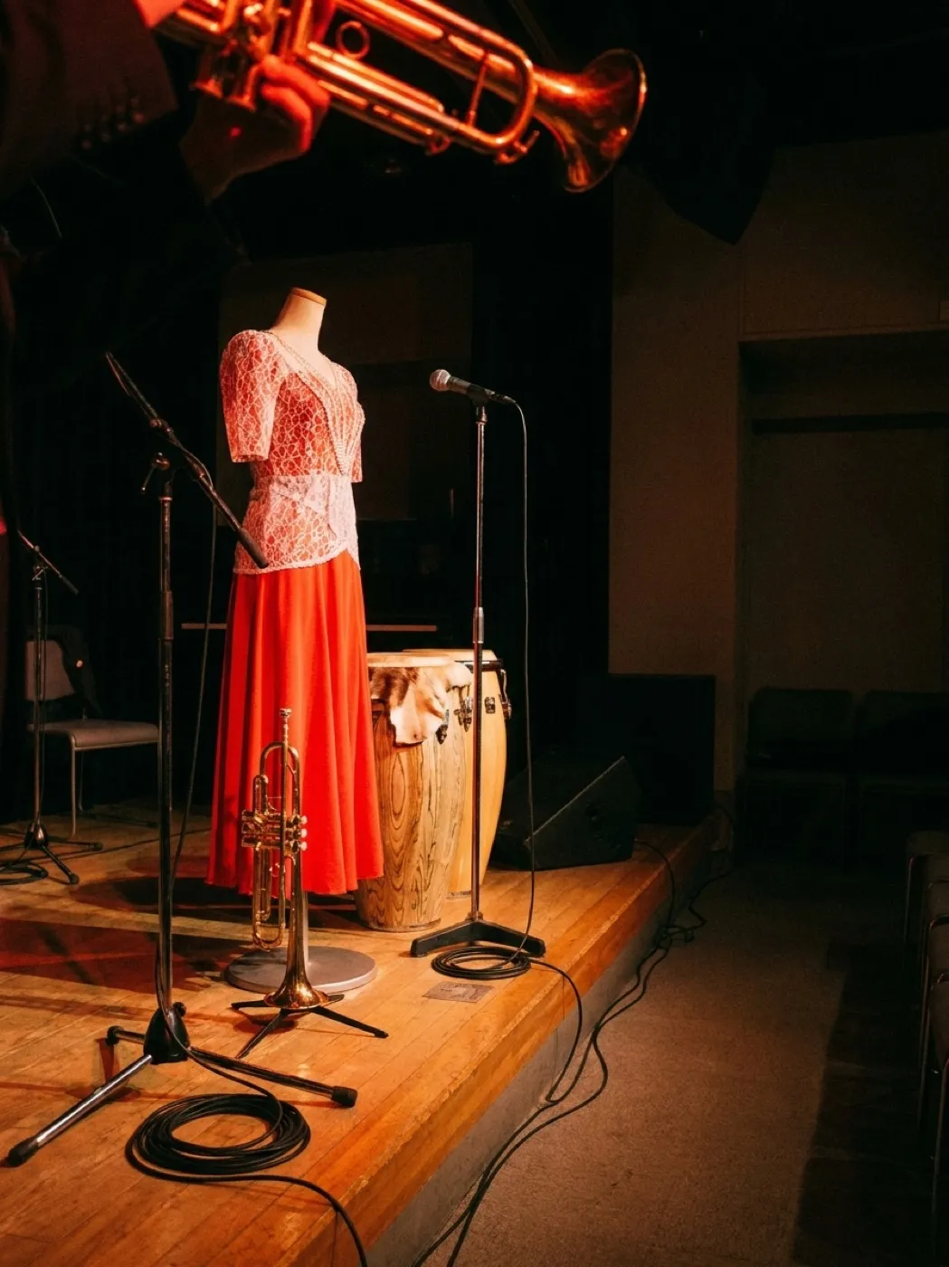 A trumpet and a pair of congas on a small raised stage under coloured lights, the room dark beyond