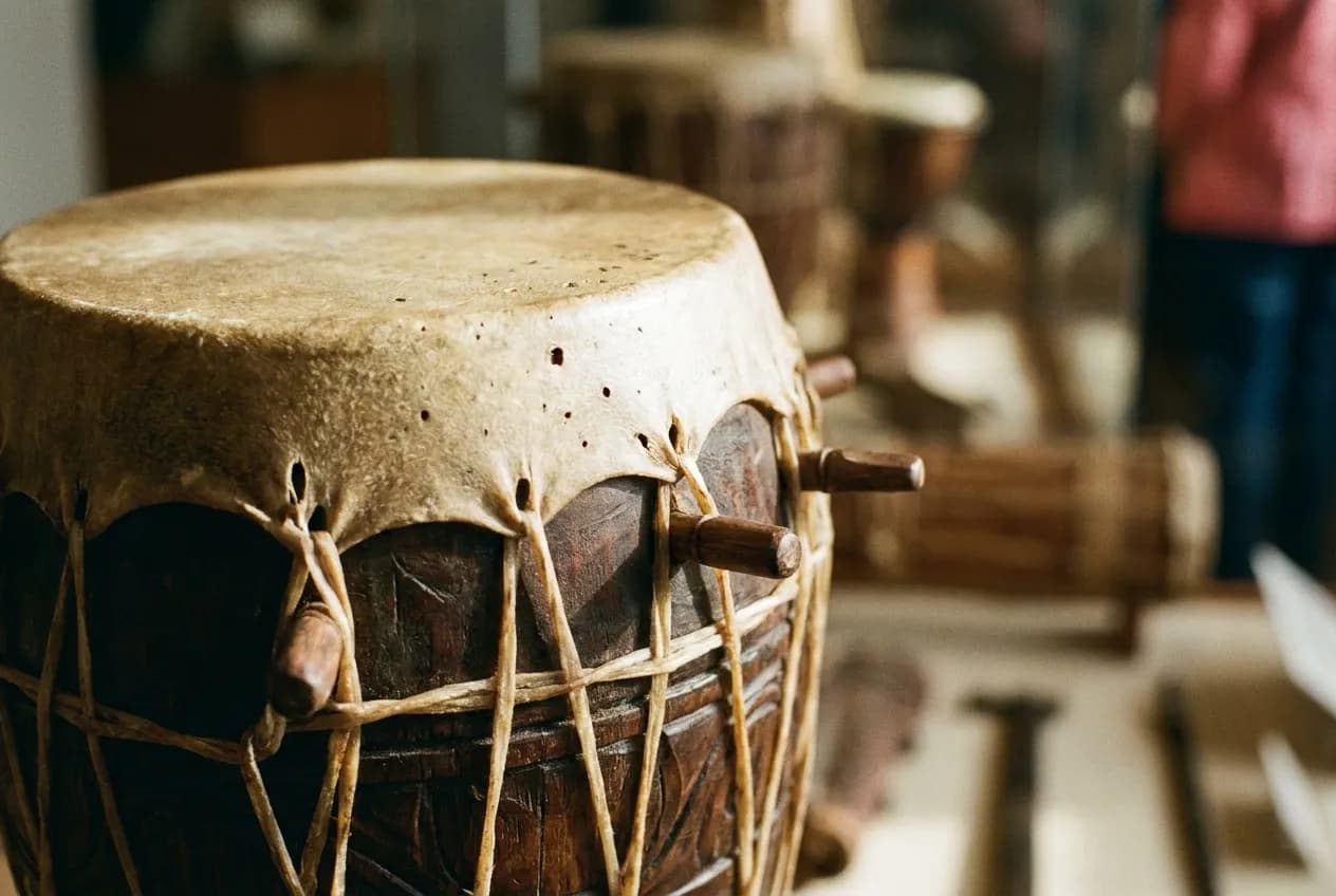 The head of a hand drum photographed close, tensioned skin and rope lacing visible against the carved wooden shell