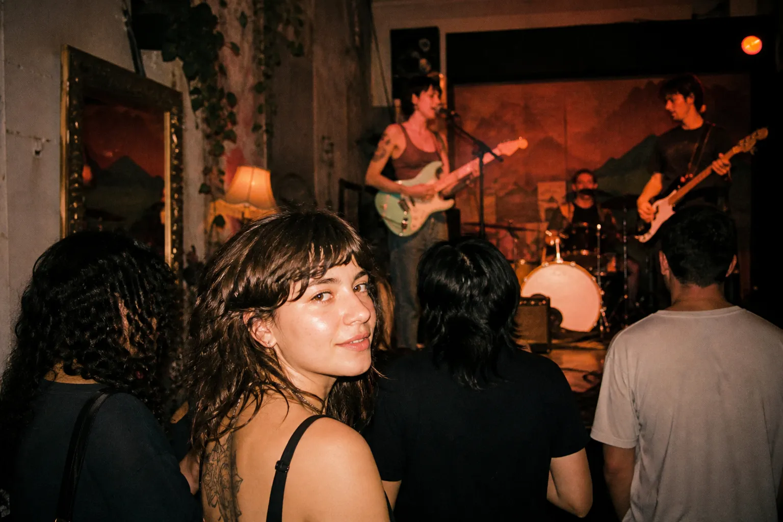 A small dimly lit music venue with a band playing on a low stage and a close crowd