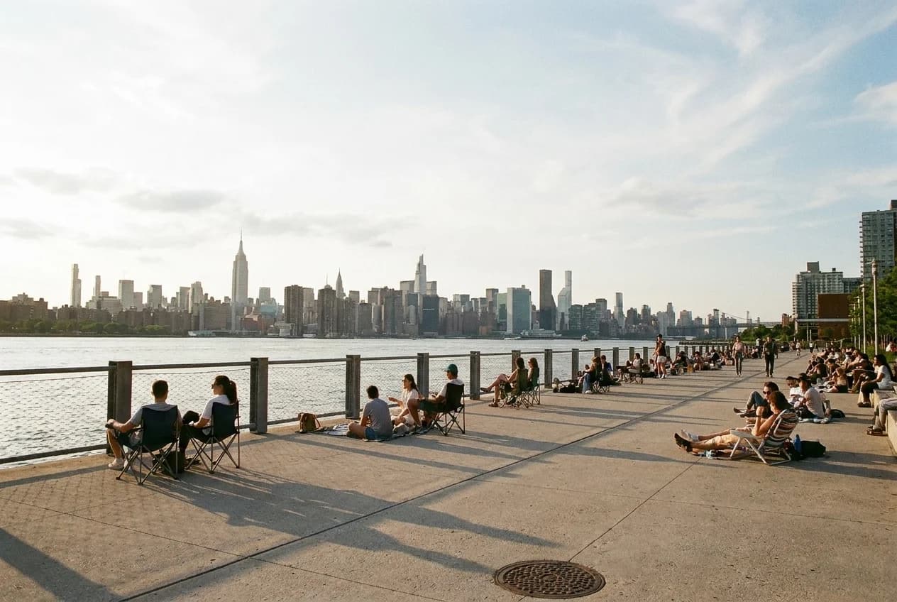 Domino Park esplanade with chairs and blankets facing East River and Manhattan skyline at sunset