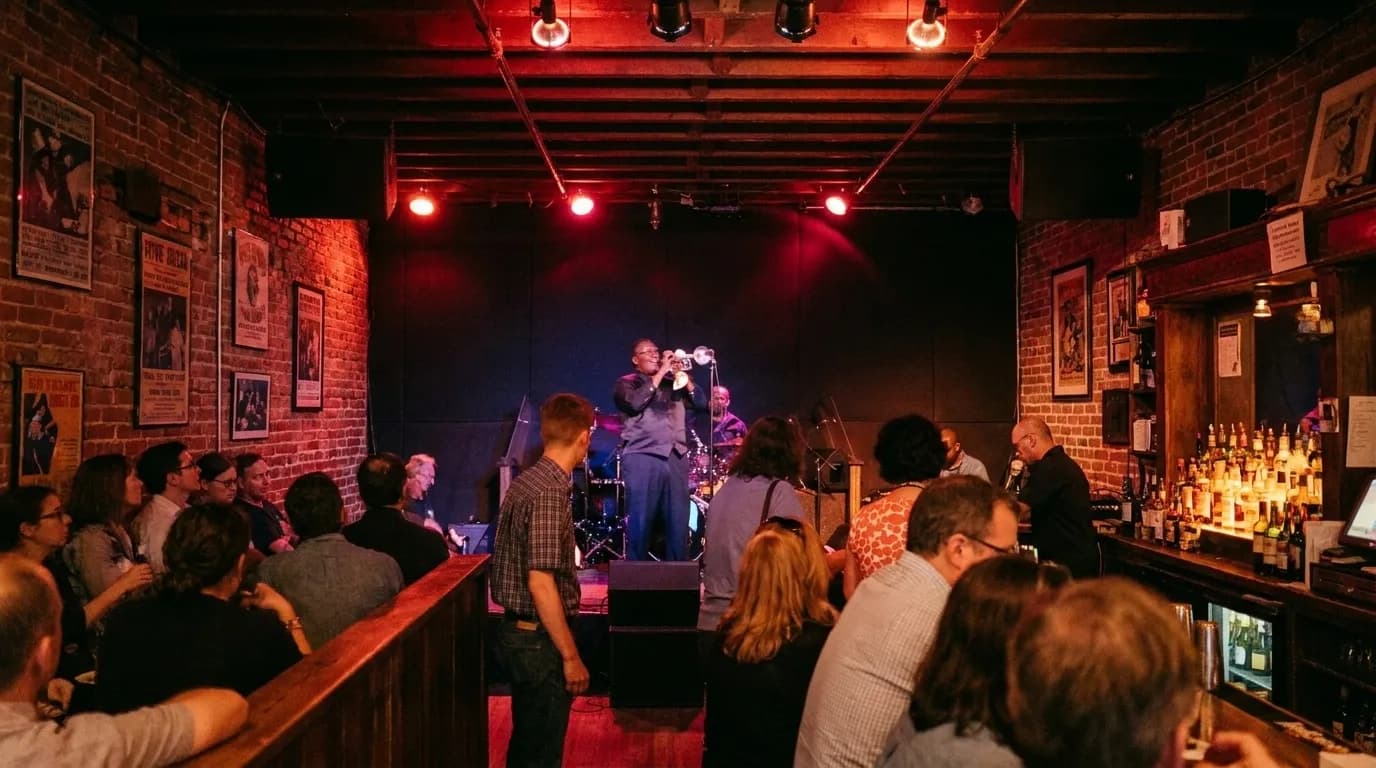 A small San Francisco bar with a band playing in the corner, red-tinted light over a horn player and drummer, a crowded bar rail and bottles glowing behind the counter