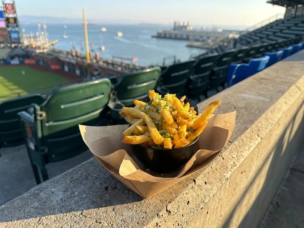 Golden garlic fries in a paper tray with McCovey Cove and San Francisco Bay visible in the background at Oracle Park