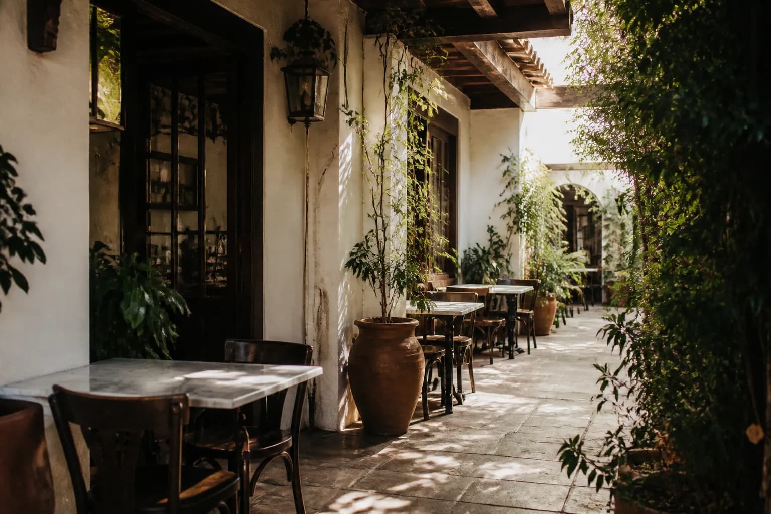 A quiet Los Angeles courtyard cafe with stucco arches, potted plants, and empty tables in morning light