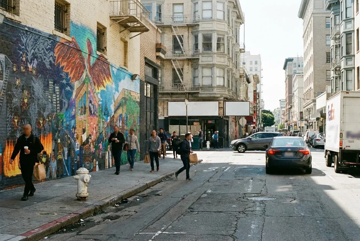 A sunny Tenderloin street corner in San Francisco with pedestrians and urban architecture during lunch hour.