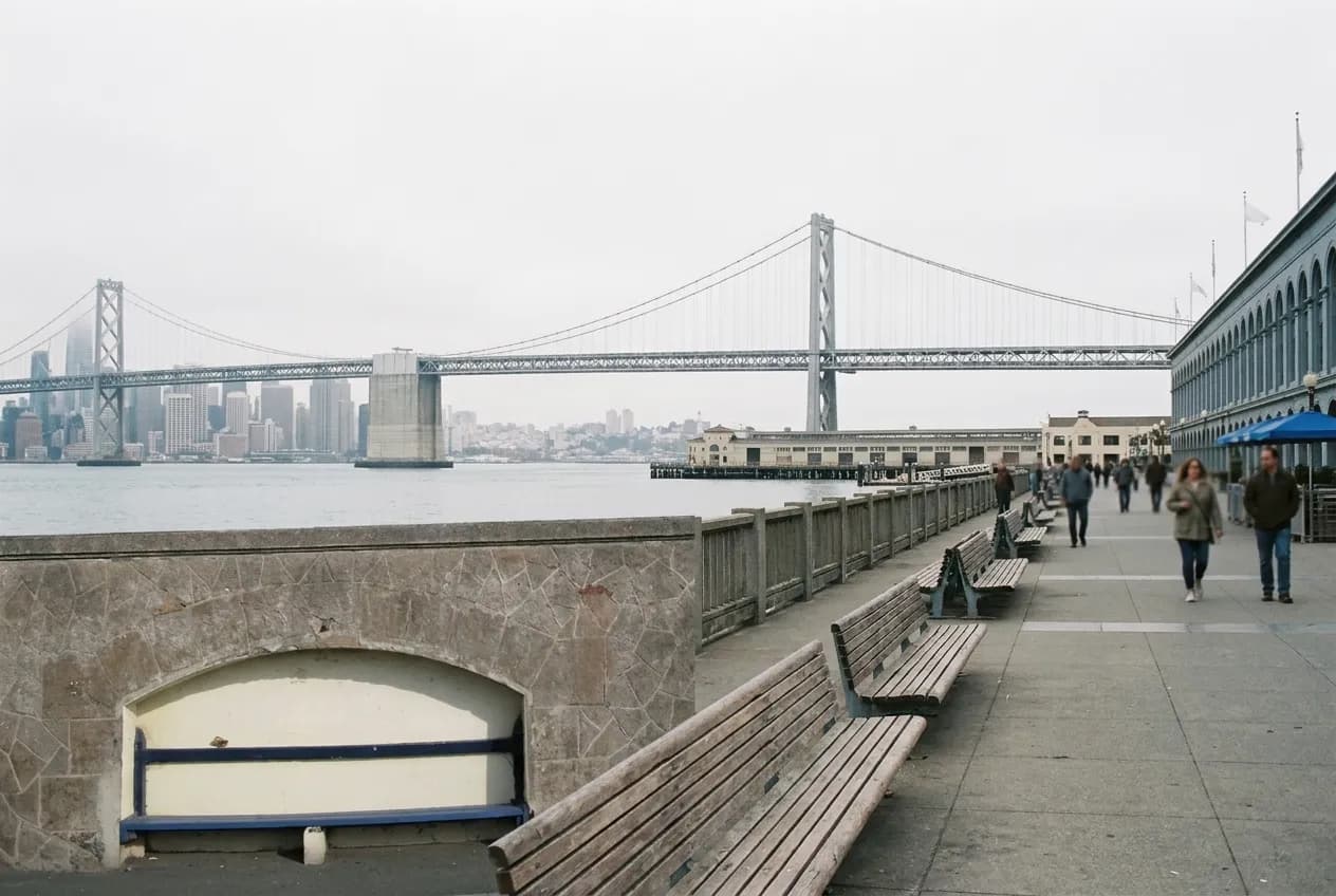 A waterfront promenade with benches looking across a bay toward a bridge