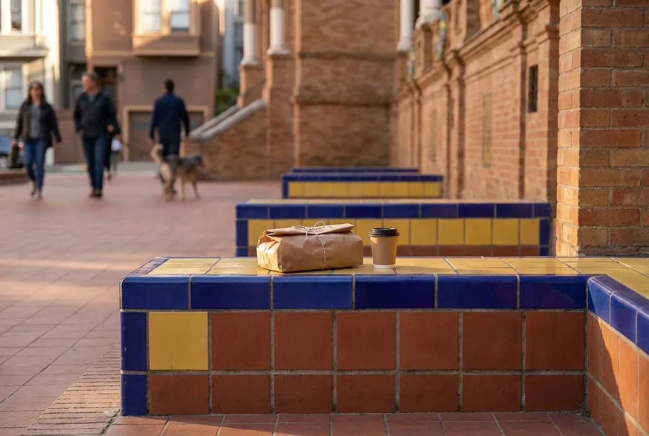 A bench in a small city plaza with a paper-wrapped lunch on it