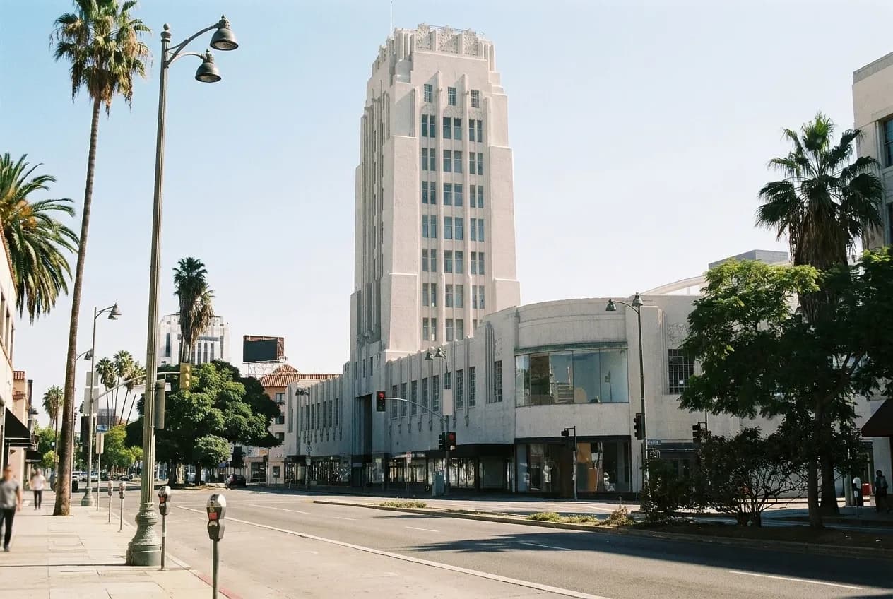 A sunlit boulevard with mid-century commercial buildings and palm trees in central Los Angeles