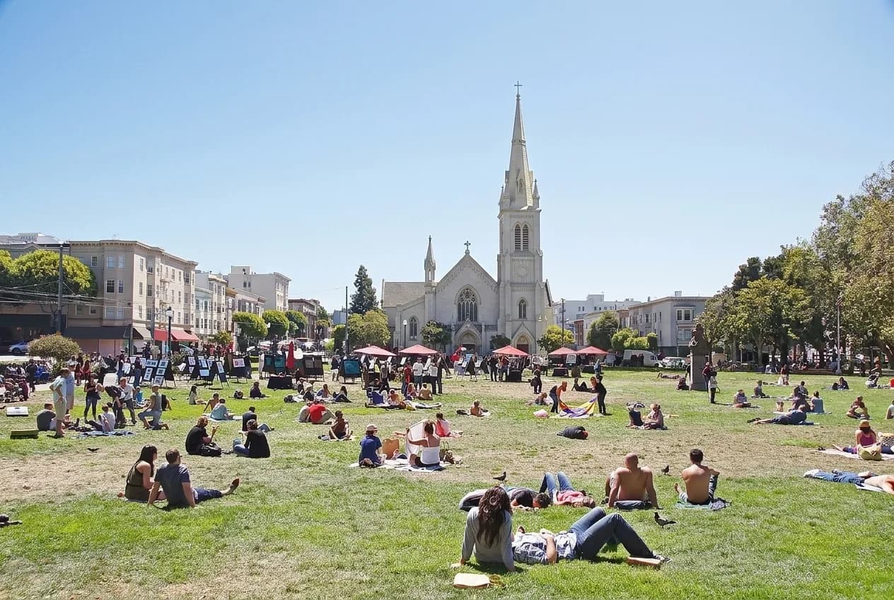 A small city park with benches and trees surrounded by low buildings and a church spire in San Francisco