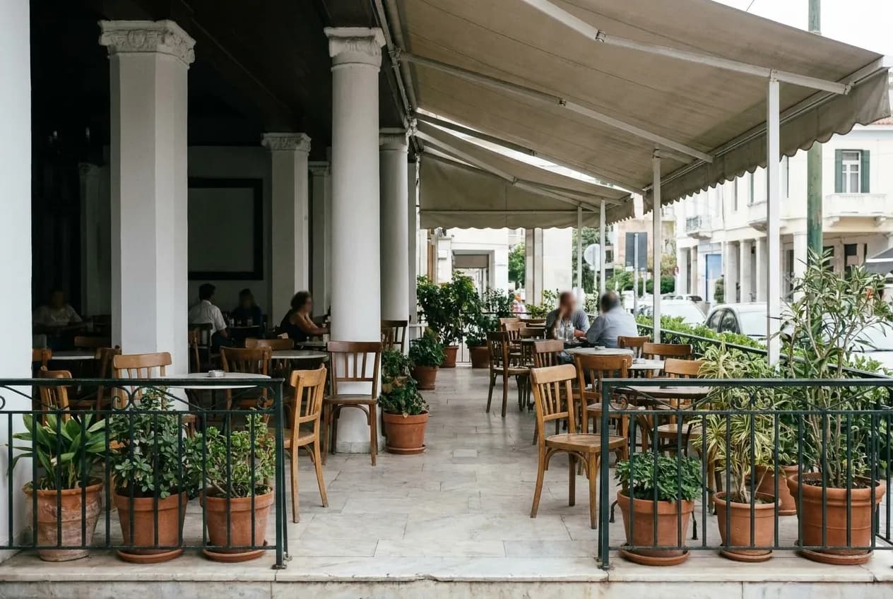 A shaded outdoor cafe patio with wooden chairs and potted plants beside a Los Angeles street